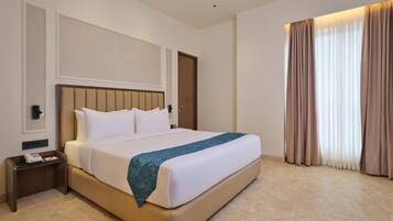 A hotel room with a large bed, a bedside table, a nightstand, a wall-mounted telephone, and a window with curtains.