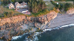 Vue aérienne d’une propriété située sur la côte, avec une grande maison, un littoral rocheux et des vagues déferlantes.
