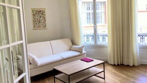 A room with a white sofa, a wooden coffee table, a window with curtains, and a floral artwork on the wall. - Paris 15 Beau 2 bedrooms, living room, ground floor. Wifi, net, Pets allowed. (Paris)