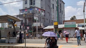 A busy urban street with a train station platform, a multi-story building with commercial signage, and pedestrians.