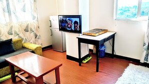 A compact living space with a sofa, a wooden table, a small TV, and a window with a city view.