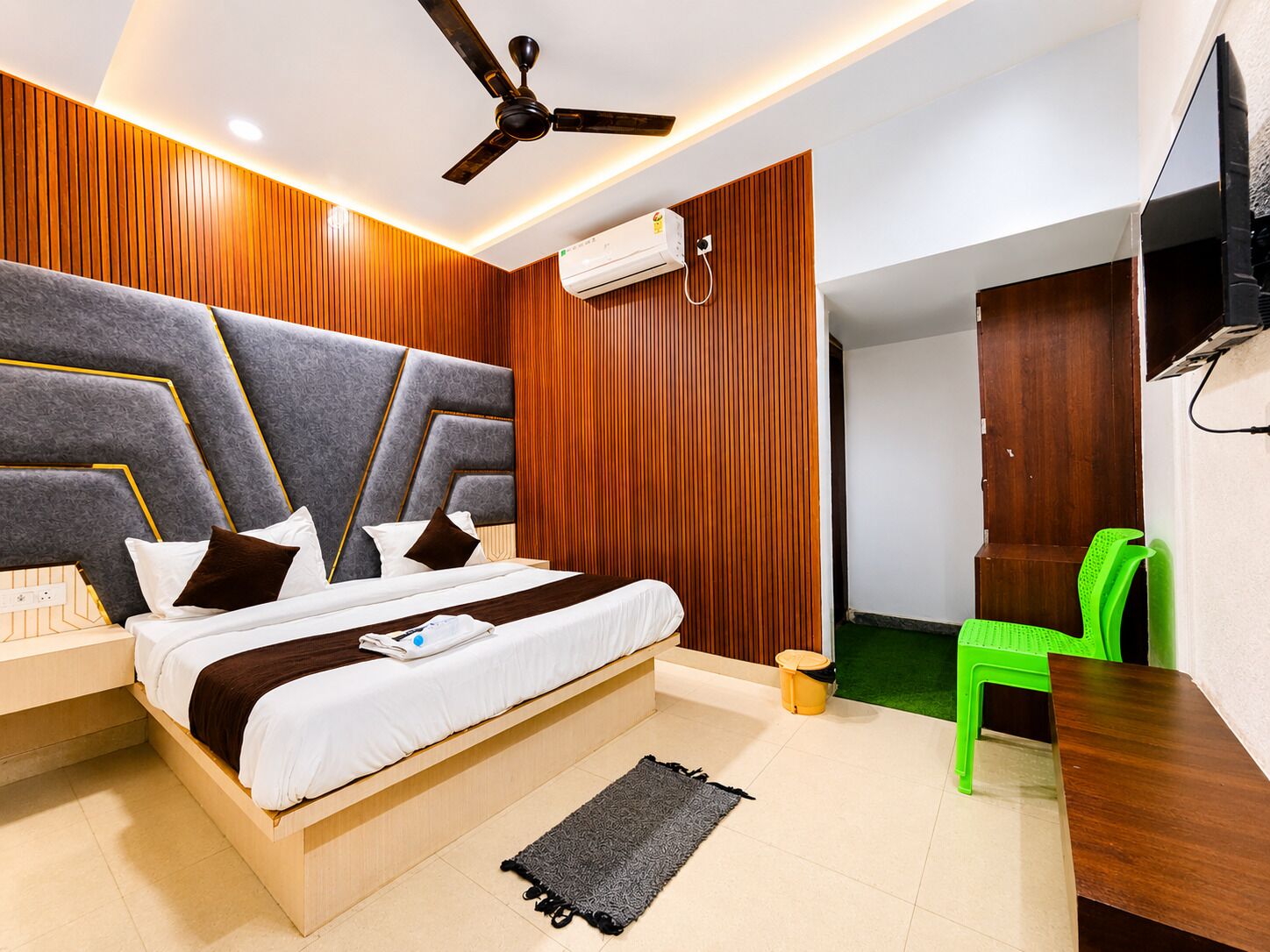 A modern bedroom with a bed, a ceiling fan, an air conditioning unit, a green chair, and a wooden wardrobe.