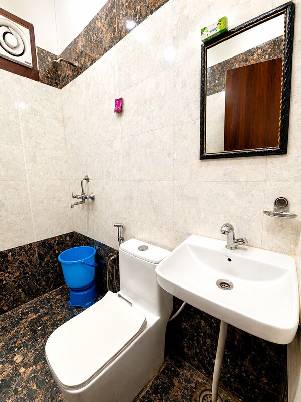 A bathroom with a toilet, bidet, sink, and a blue bucket.