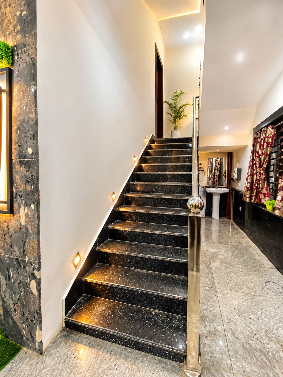Una escalera moderna con barandilla de vidrio que lleva a un rellano con una planta en maceta.