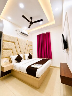 A modern hotel room with a bed, a ceiling fan, an air conditioning unit, a TV, and a window with curtains.