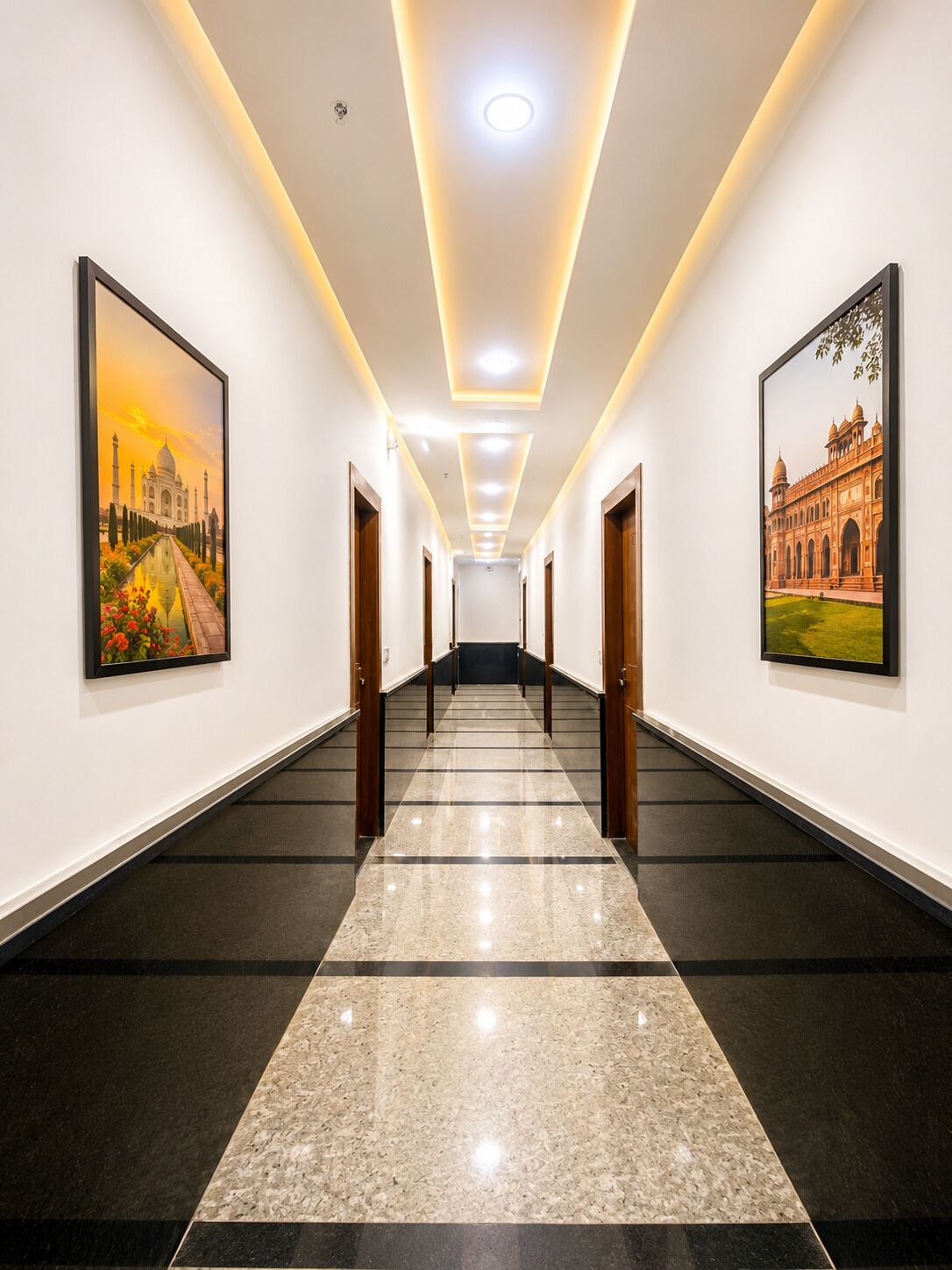 Un pasillo de hotel con piso de mármol, cuadros en las paredes y una escalera al final.