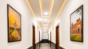 A hotel corridor with a marble floor, framed pictures on the walls, and a staircase at the end. - Hotel Mero Vrindavan (Vrindavan)