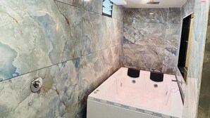 A bathroom with a marble wall, a white toilet, a bathtub, and a blue trash bin. - Hotel kings villa (Ahmedabad)