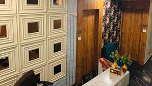 A hotel reception area with a marble counter, a red cloth, and a wall with decorative panels. - Hotel kings villa (Ahmedabad)