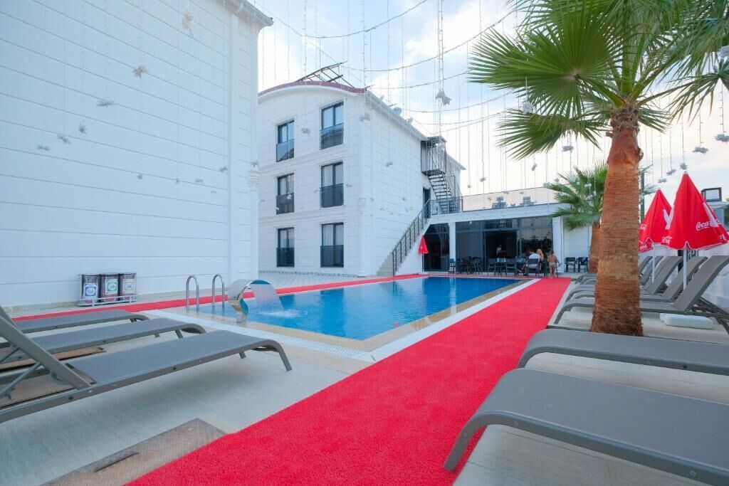 A pool area with a red carpet, lounge chairs, a palm tree, and a building with balconies.