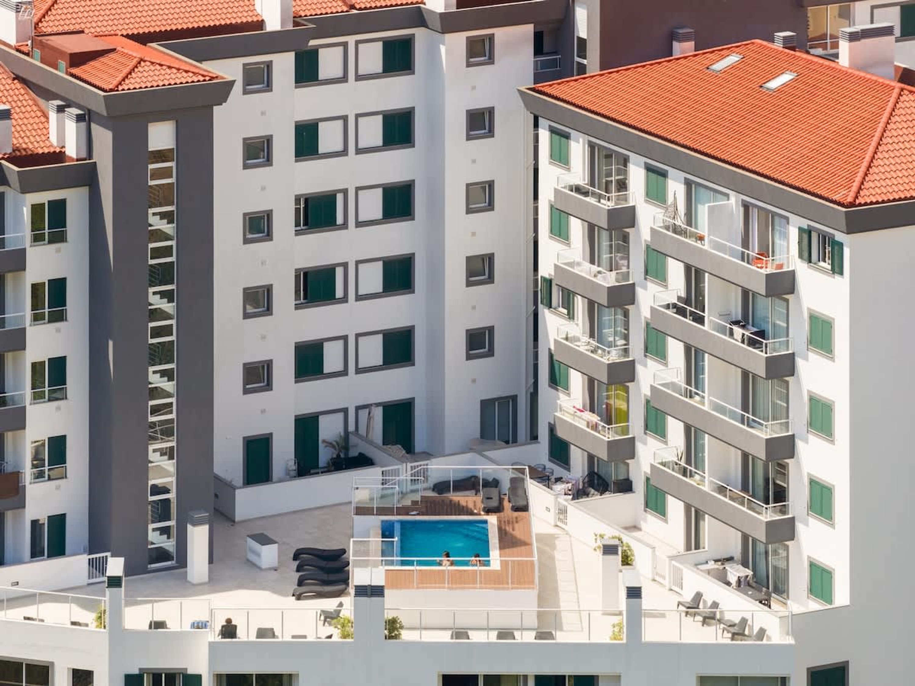 Un edificio residencial de varios pisos con balcones, piscina en la azotea y tejado de tejas rojas.