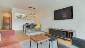 Ein modernes Wohnzimmer mit einer Couch, einem Couchtisch, einem Fernseher und einem Essbereich mit Stühlen und einem Tisch.
