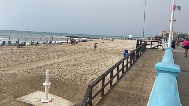 A beach with a wooden pier, beach chairs, umbrellas, and people. - Fabi Beach Apartment (Torrevieja) (Torrevieja)