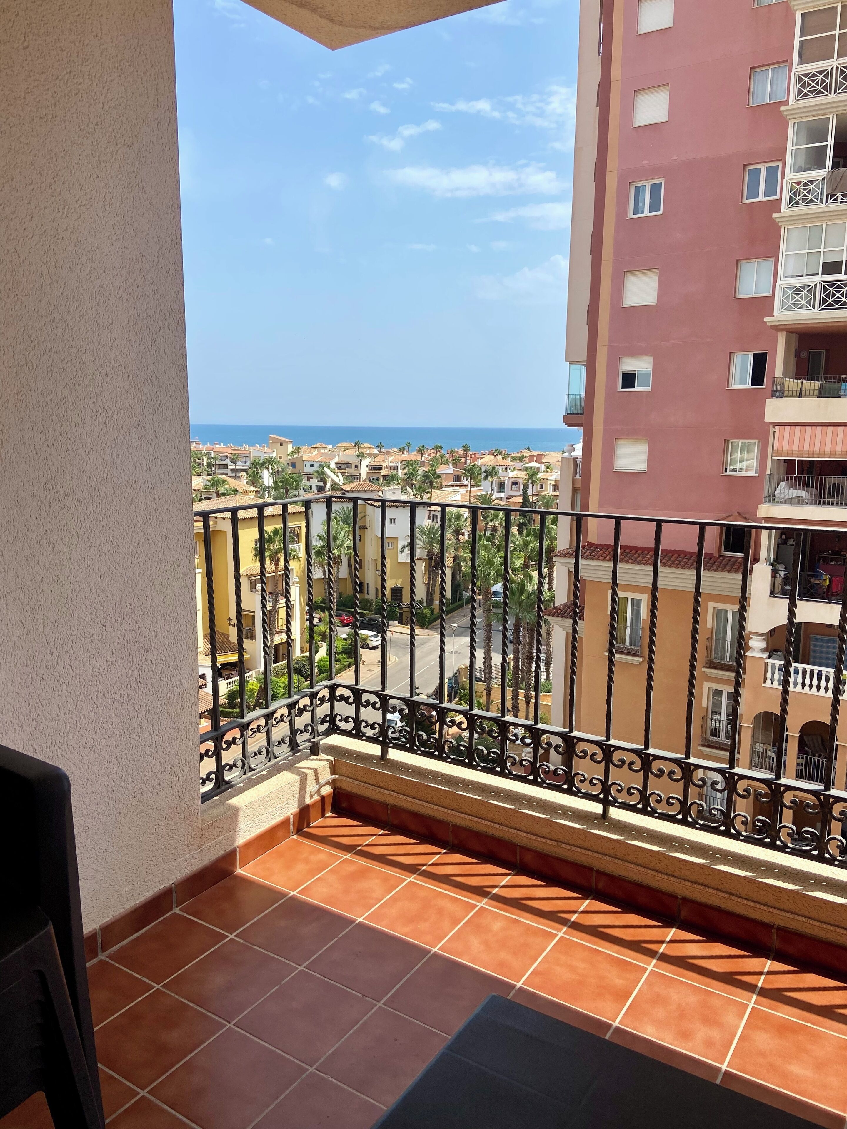 A balcony with a view of a coastal town, featuring tiled flooring and a metal railing.