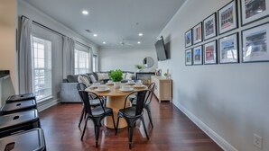 Un salon spacieux comprenant un coin repas, un canapé et un téléviseur fixé au mur.
