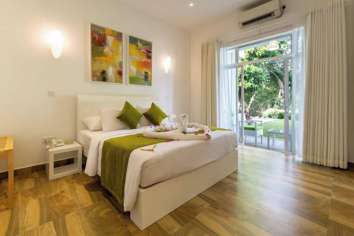 A hotel room with a large bed, a bedside table with a phone, and a view of the outdoors through a sliding glass door.