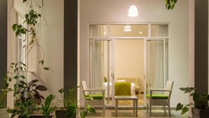 A hotel entrance with a glass door, two white chairs with green cushions, and potted plants.