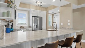 A modern kitchen with a large island, stainless steel appliances, and bar stools. - Kiva Dunes Lodge Unit 405 (Gulf Shores)