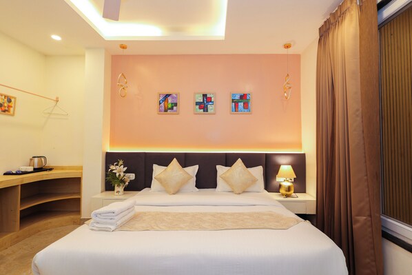 A hotel room with a large bed, a bedside table with a lamp, a wall with abstract art, and a window with curtains.