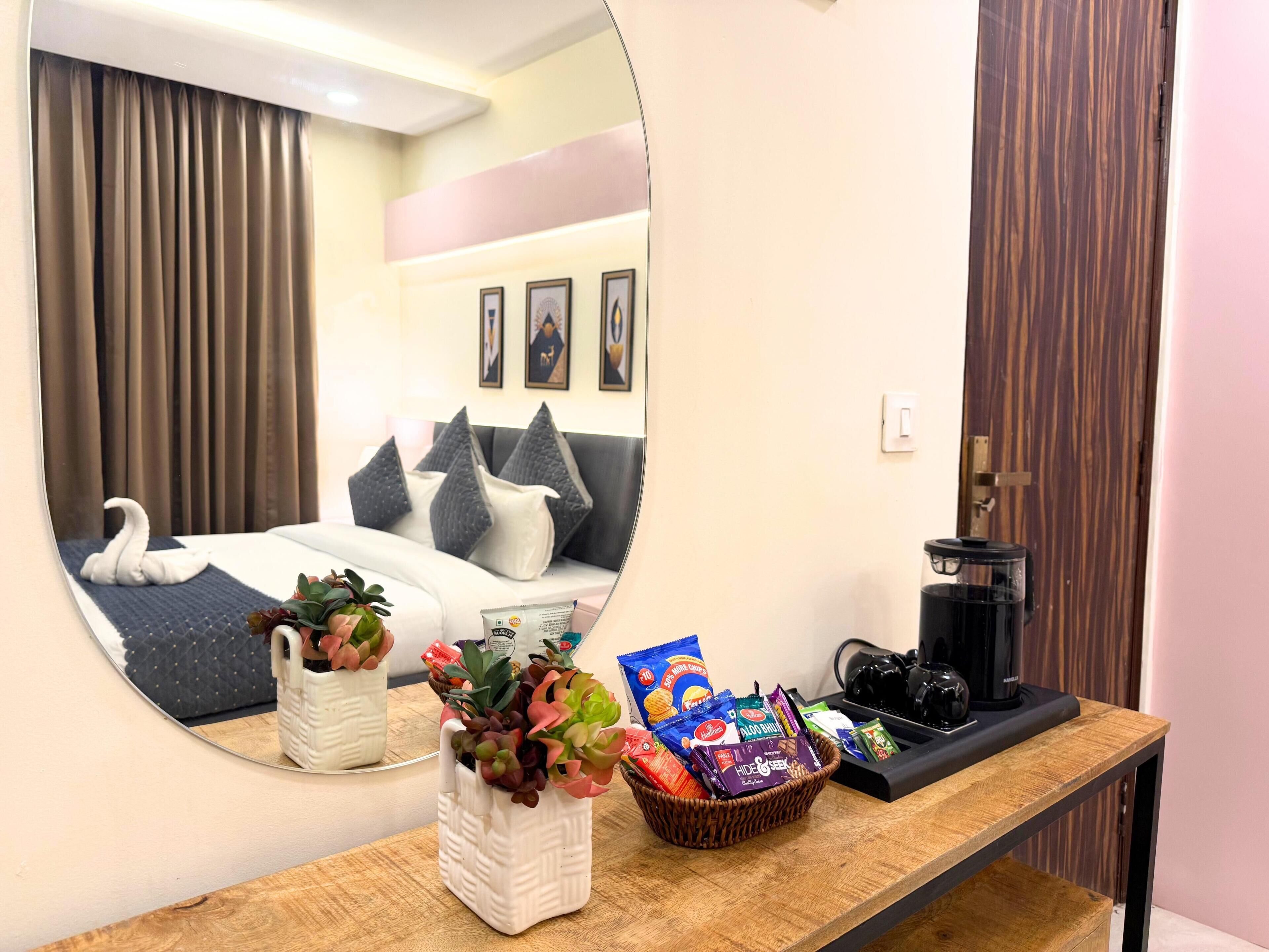 A hotel room with a large mirror reflecting the bed, a bedside table with snacks, a coffee maker, and a potted plant.