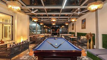 A pool table in a room with a patterned floor, ceiling fans, and hanging lights.
