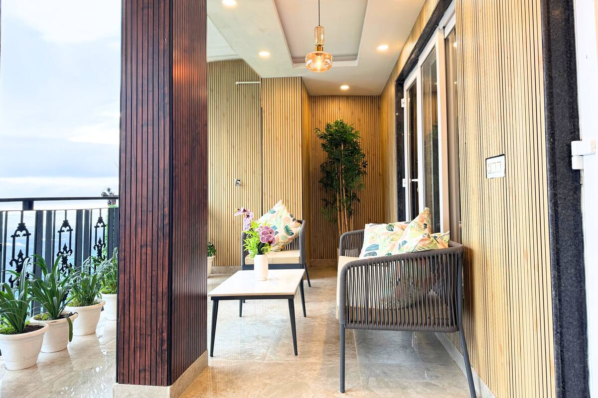 Un balcón con un muro de madera, una silla de mimbre, una mesa y plantas en macetas.