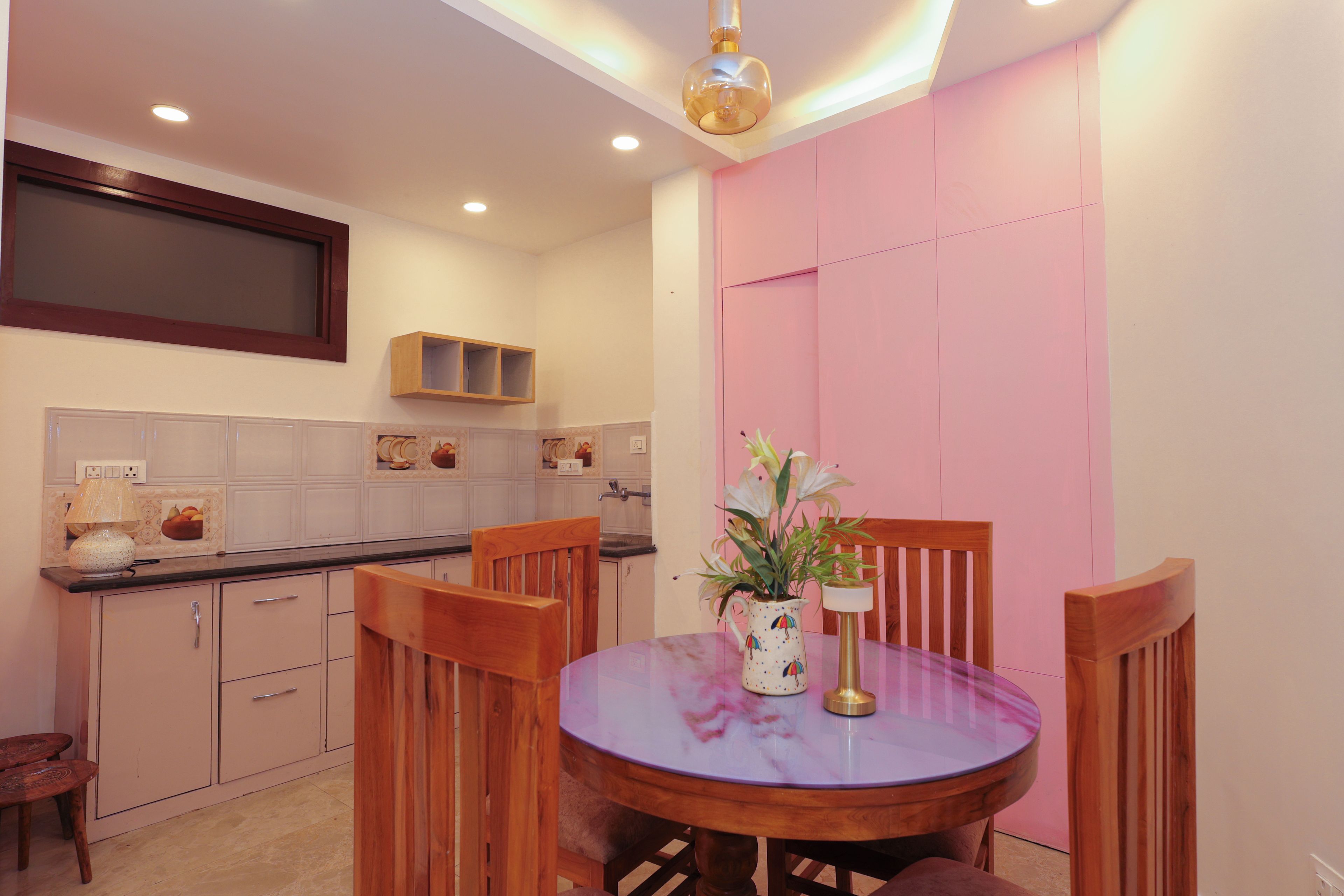 Un comedor con una mesa redonda, sillas, un jarrón con flores y una lámpara sobre la mesa.
