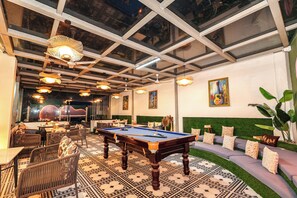 A pool table in a room with a high ceiling, patterned floor, and seating area.