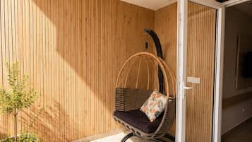 Un interior moderno con un muro de listones de madera, una silla colgante con cojín, una planta en maceta y un cerramiento de vidrio corredera que da a otra habitación.
