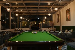 Ein Billardtisch mit Kugeln, umgeben von Sitzgelegenheiten und Tischen, mit hängenden Lampen und Kunstwerken an den Wänden.