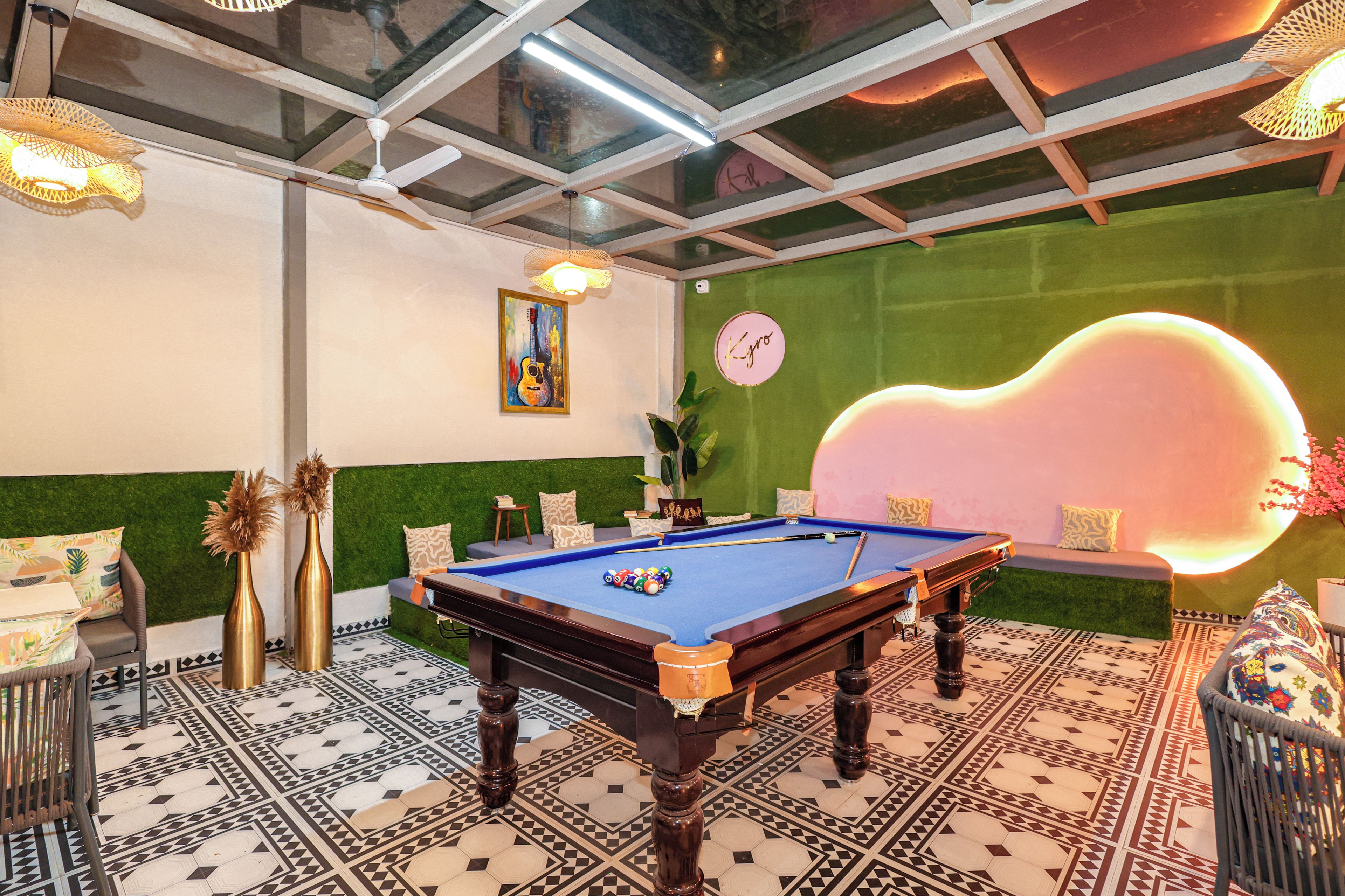 Una mesa de billar en una habitación con suelo estampado, pared verde y un reloj.