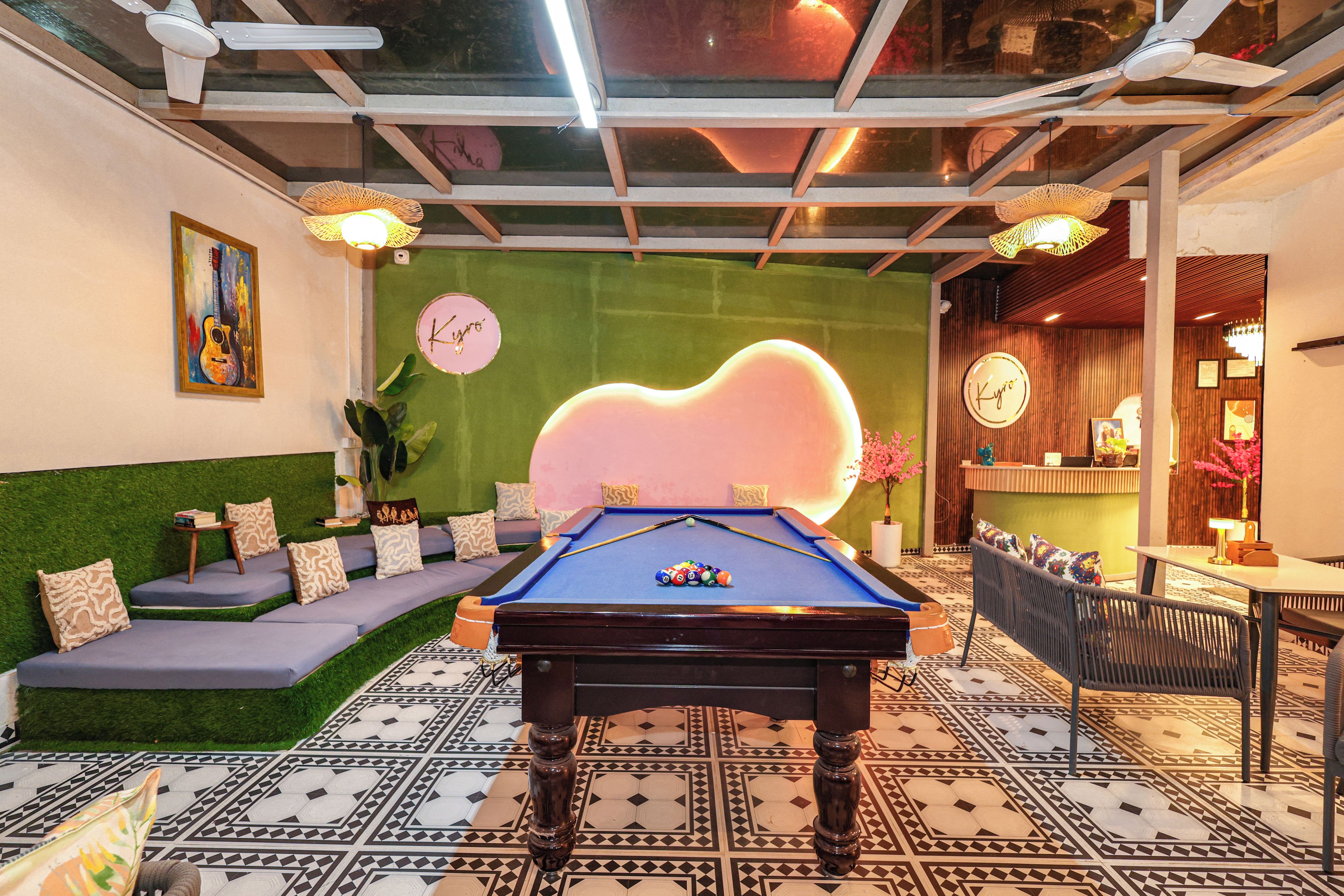 Una mesa de billar en una habitación con pared verde, un reloj y una zona de bar.