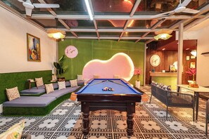 Une table de billard dans une pièce avec un mur vert, une horloge et un coin bar.