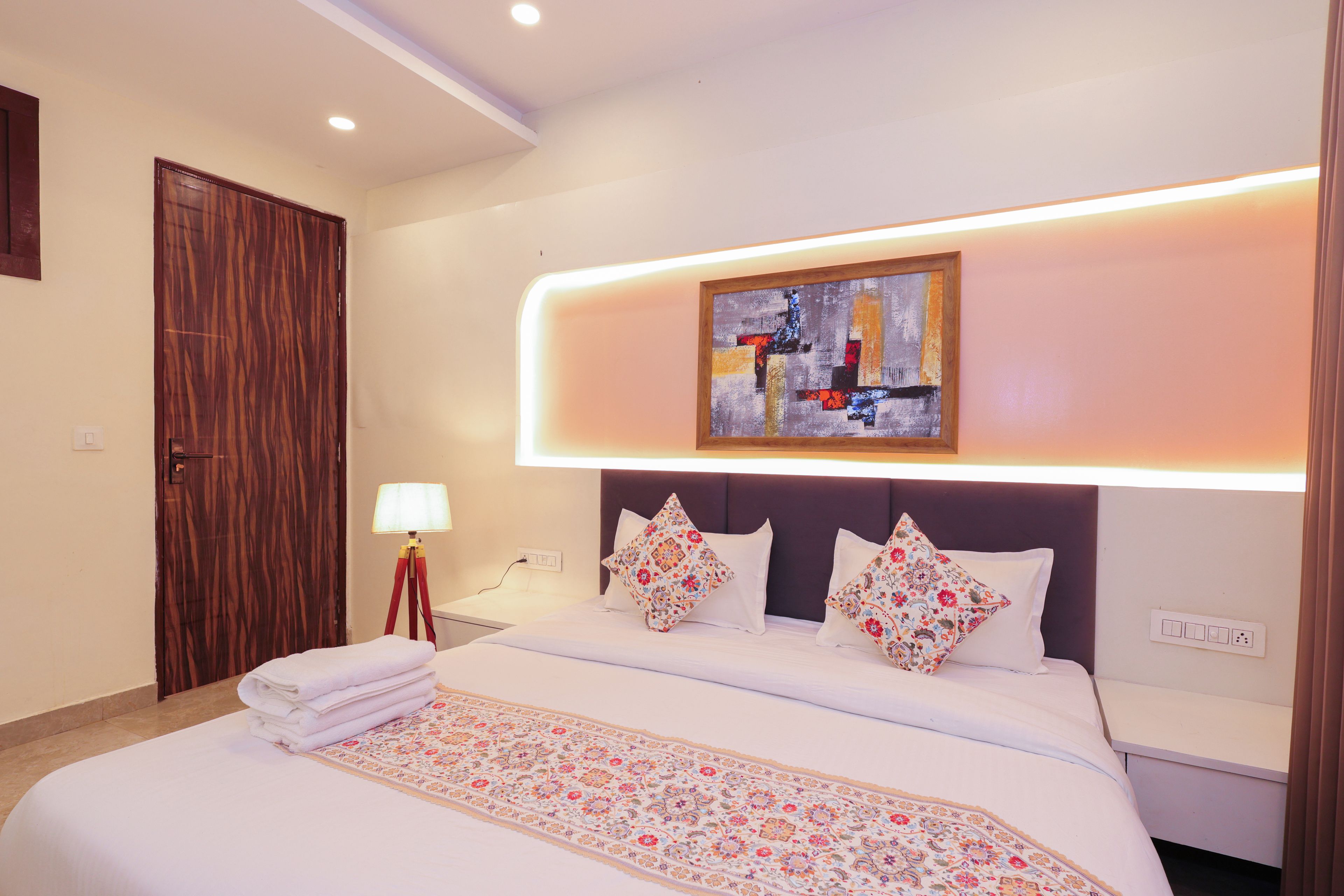 Habitació d'hotel amb un llit, una tauleta de nit, una làmpada, un quadre i una porta.