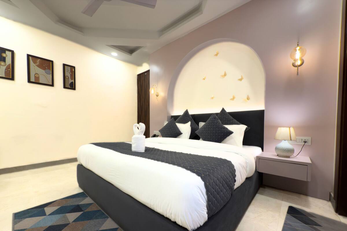 Habitación de hotel moderna con una cama grande, una mesita de noche, una lámpara y una alfombra de diseño geométrico.