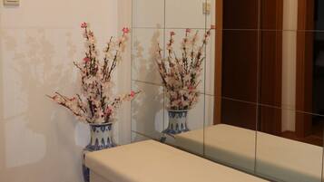 A bathroom with a mirror, two vases with flowers, a wooden bench, and a tiled wall.