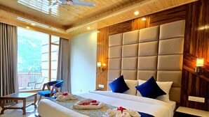 Une chambre d’hôtel dotée d’un grand lit, d’un ventilateur de plafond, d’une tête de lit en bois, d’un coin salon avec une table et des chaises, et offrant une vue sur l’extérieur.