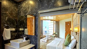 Une salle de bain moderne avec un grand miroir, un lavabo blanc et un lit recouvert de draps blancs et agrémenté d’oreillers verts.