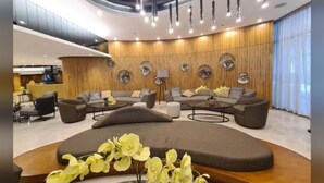 A modern hotel lobby with a curved seating area, wooden panel walls, and a central light fixture.