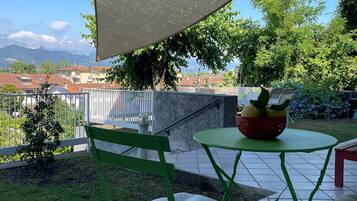 Une terrasse extérieure avec une table et des chaises, un espace ombragé et une vue sur une ville et des montagnes en arrière-plan.