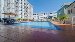 A swimming pool with tiled flooring, lounge chairs, and potted plants.