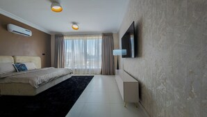 A modern hotel room with a bed, a flat-screen TV mounted on the wall, a bedside table, and a large window with curtains.