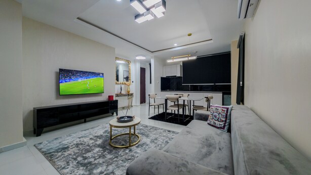 A modern living room with a flat-screen TV, a sofa, a coffee table, and a dining area.