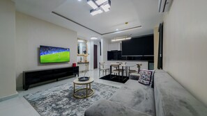A modern living room with a flat-screen TV, a sofa, a coffee table, and a dining area. - Luxe 1BR Retreat in Ikoyi • Pool • Fast WiFi • Near Beach (Ikoyi)