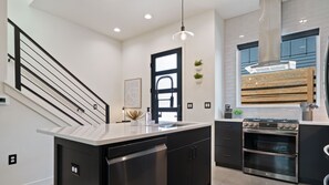 Una cucina moderna con isola centrale, mobili neri, elettrodomestici in acciaio inossidabile e zoccolo in legno.