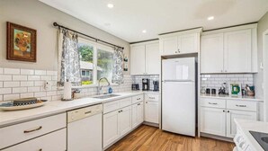 A modern kitchen with white cabinets, a built-in dishwasher, and a refrigerator. - Cape Escape - New Oceanfront Listing! (Arch Cape)
