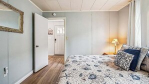A bedroom with a bed, a nightstand, a lamp, and a door leading to another room. - Cape Escape - New Oceanfront Listing! (Arch Cape)
