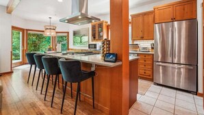 A modern kitchen with wooden cabinets, a stainless steel refrigerator, and a central island with bar stools.