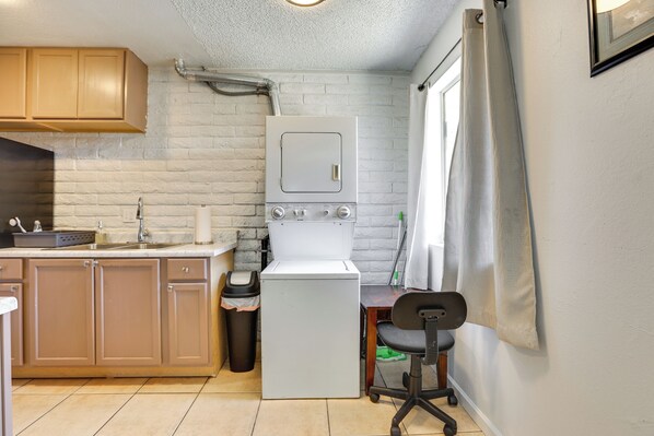 Une cuisine compacte équipée d’un lave-linge et d’un sèche-linge intégrés, de meubles en bois, d’une poubelle et d’un petit bureau avec une chaise.
