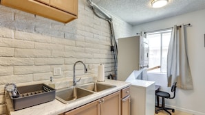 Una cocina con pared de ladrillo, un lavamanos, lavavajillas y una ventana con cortinas.